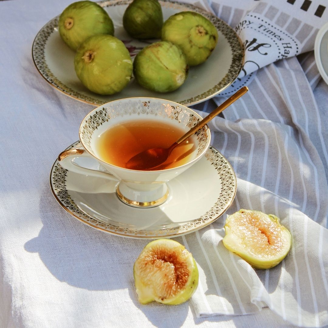 Image of a cup of tea and a plate of figs on a linen table spread.